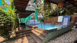 Une piscine extérieure avec des marches menant à l’eau, entourée de verdure et dotée d’un sol carrelé.