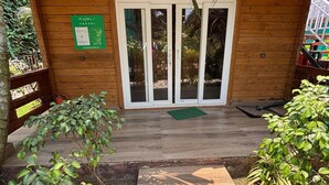 Un bâtiment en bois avec une entrée dotée d’une porte en verre, entouré de verdure et bordé d’un chemin pavé.