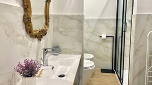 Un baño moderno con lavamanos de mármol, espejo con marco dorado y cabina de ducha de vidrio.