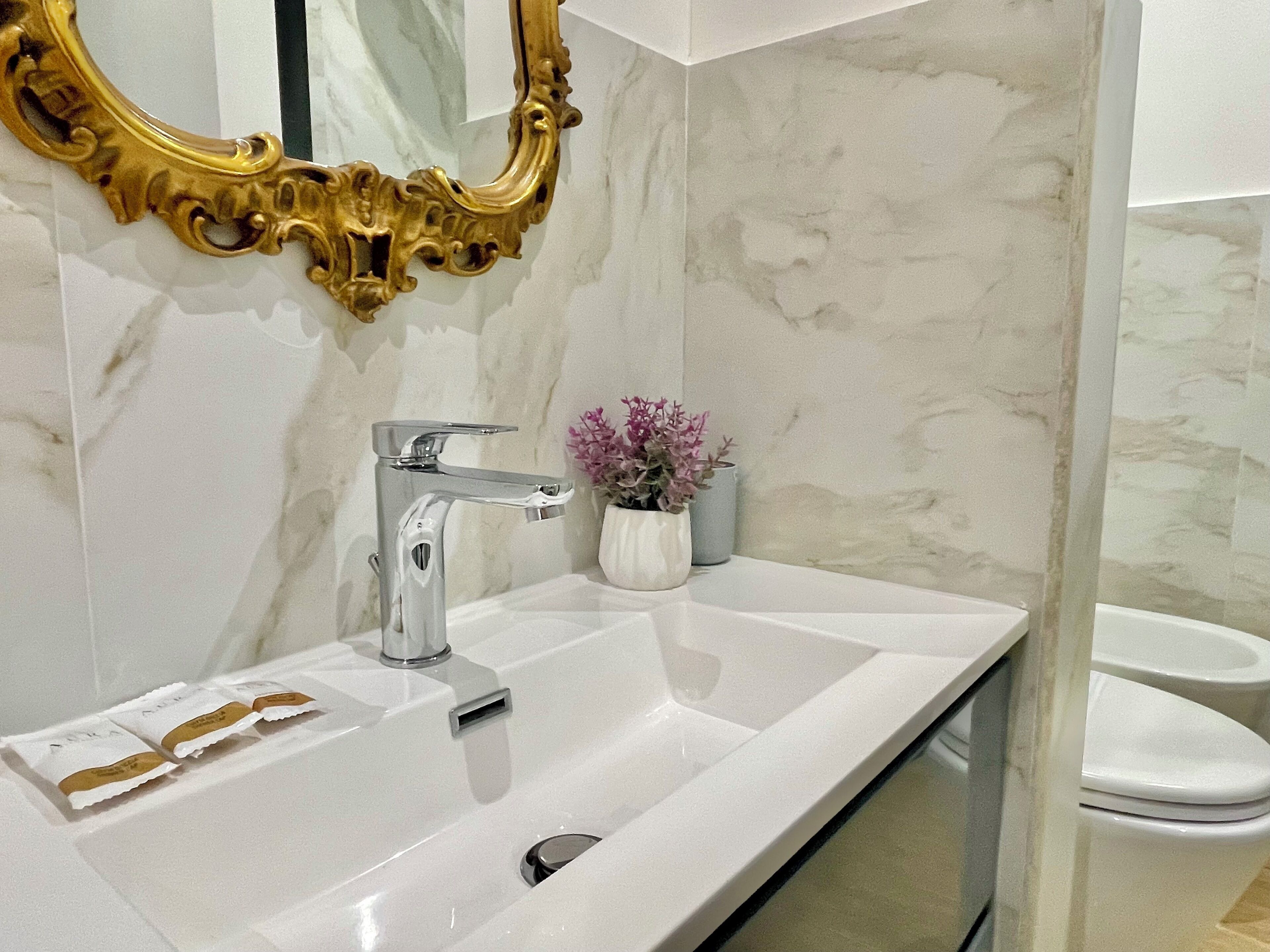 A bathroom with a white sink, a gold-framed mirror, and a marble wall.