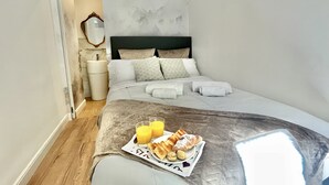 Una cama bien hecha con un carrito de desayuno, una mesita de noche y un espejo en la pared.