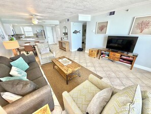 A living room with a sofa, coffee table, TV stand, and kitchen in the background.