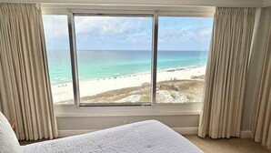 A hotel room with a large window offering a beach view, a bed, and curtains. - Beach front Gulf Views Golf Cart 4112 BS1 (Miramar Beach)