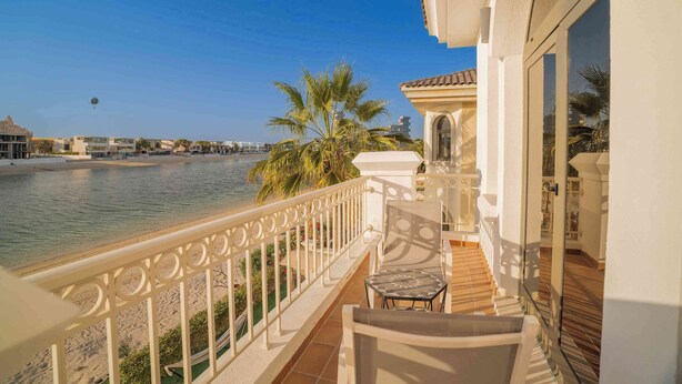 Un balcón con vista al mar, una palmera y una silla.