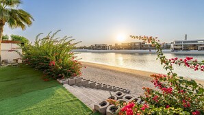 Una propiedad frente al mar con un paseo pavimentado, una palmera y plantas con flores.