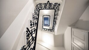 A narrow stairwell with a small window at the top, white walls, and a black metal railing. - Prime West End Flat – Walk to Everything! (Greater London)