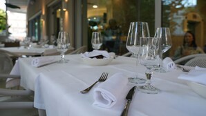 Una mesa de restaurante dispuesta con manteles blancos, copas de vino y cubiertos.