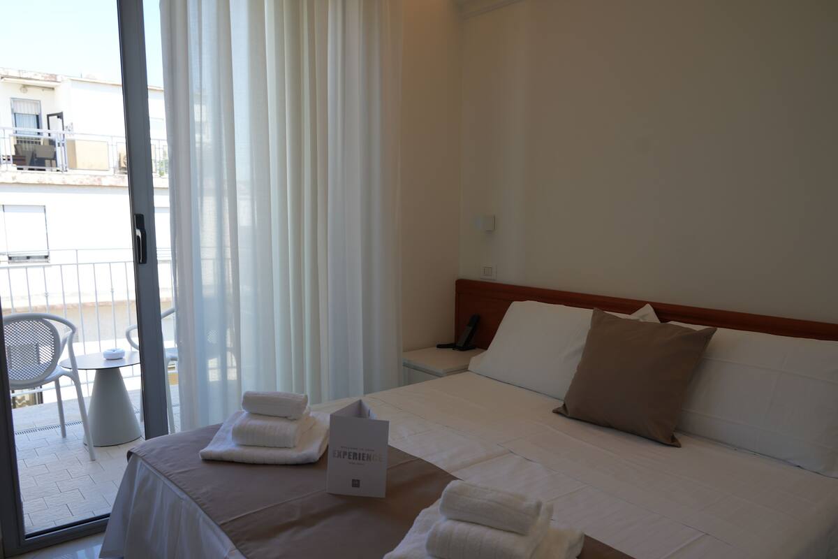 A hotel room with a bed, pillows, a sign, and a table with towels.
