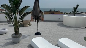 Terraza en la azotea con sillones de descanso, plantas en macetas y vistas al mar.