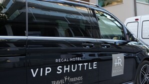 Una camioneta negra con la marca "Regal Hotel" y "Travel Friends" estacionada frente a un edificio de diseño moderno y con balcón.