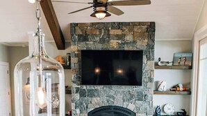 A cozy living room with a stone fireplace, a ceiling fan, and a flat-screen TV mounted above it.