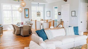 A spacious living room with a white sofa, wicker chairs, and a dining area with a table and chairs.