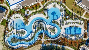 An aerial view of a resort with a large central pool, multiple smaller pools, and palm trees.