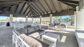 An outdoor patio area with white furniture, including sofas and tables, under a covered roof structure.