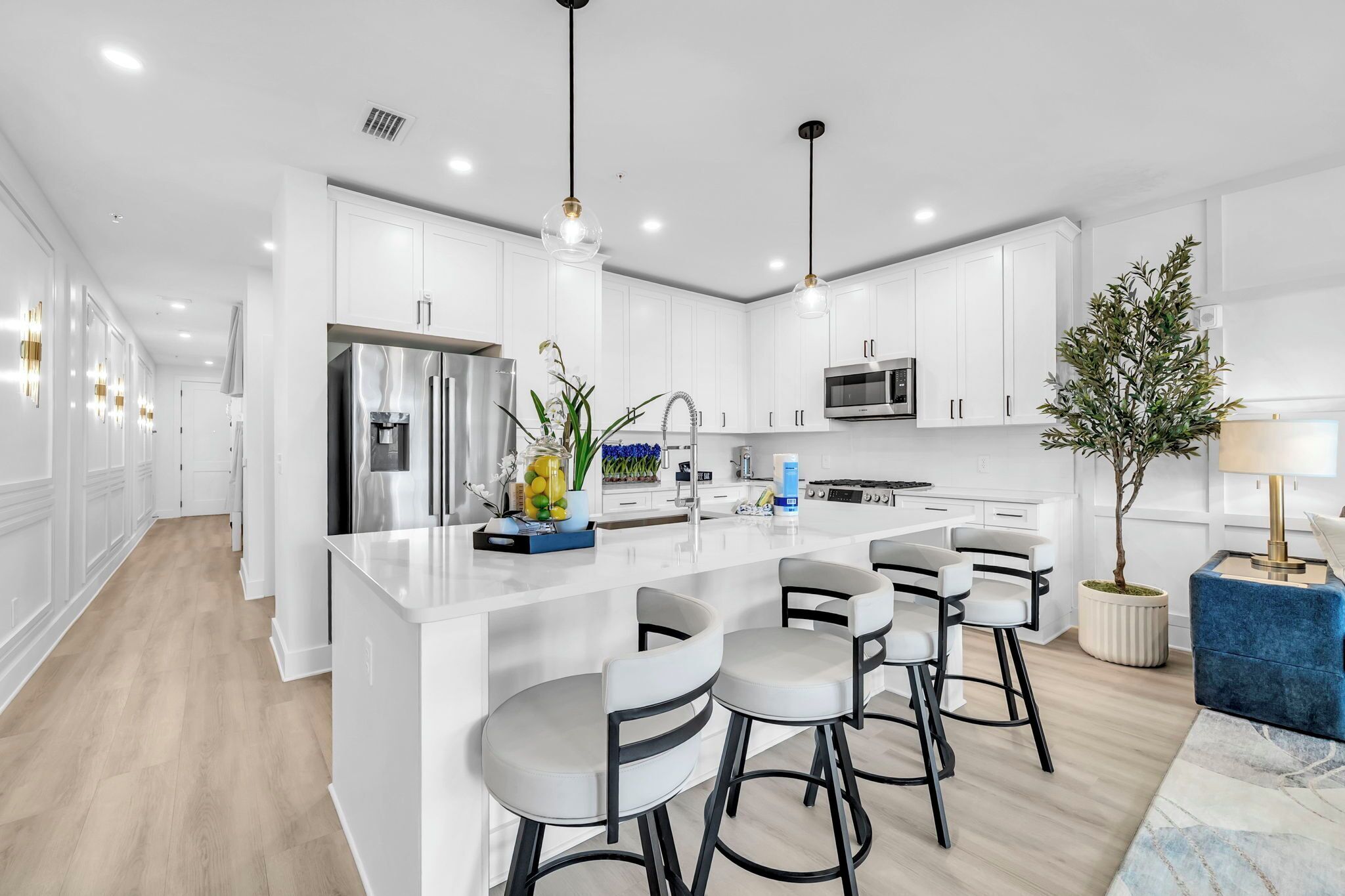 A modern kitchen with white cabinetry, a central island with bar stools, stainless steel appliances, and pendant lighting.