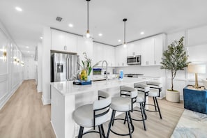 A modern kitchen with white cabinetry, a central island with bar stools, stainless steel appliances, and pendant lighting.