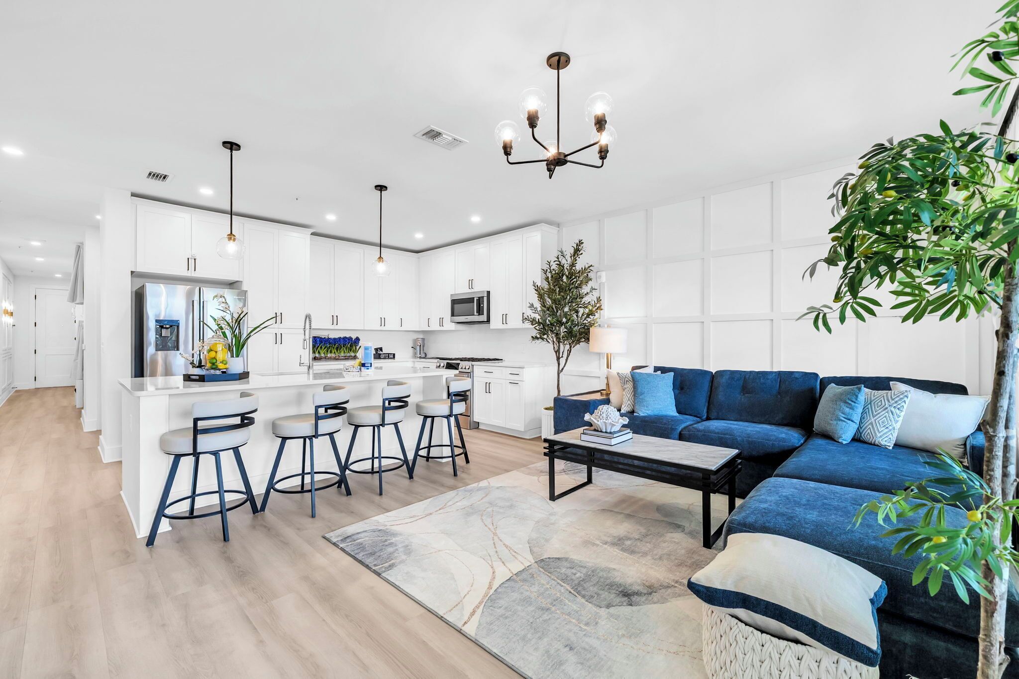 A modern kitchen with white cabinetry, a central island with bar stools, a blue sofa, and a chandelier.