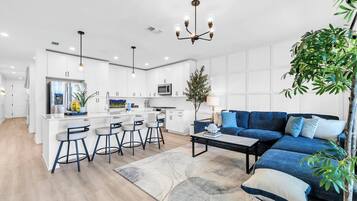 A modern kitchen with white cabinetry, a central island with bar stools, a blue sofa, and a chandelier.