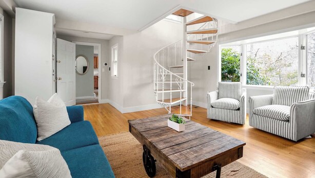 A spacious living room with a wooden coffee table, a blue sofa, striped armchairs, and a white spiral staircase. - 2 Miles to Coast Guard Beach! (Eastham)