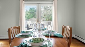 A dining area with a wooden table set for four, chairs, and a view of a balcony with outdoor furniture. - 2 Miles to Coast Guard Beach! (Eastham)