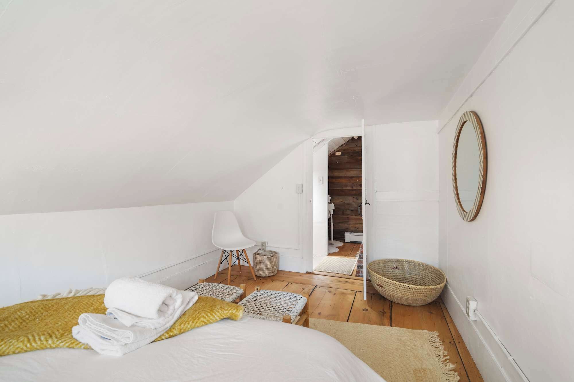 Een slaapkamer met een bed, een stoel, een spiegel en een kleine badkamer zichtbaar door een geopende deur.