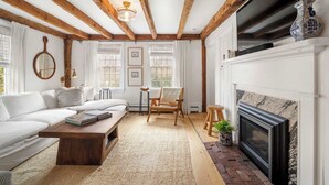 Una sala de estar acogedora con un sofá blanco, una mesa de centro de madera, una chimenea y un televisor montado encima.