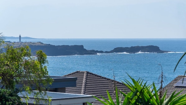 A coastal view with a lighthouse, rocky coastline, and residential buildings with solar panels.