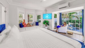 A spacious bedroom with a large bed, two seating areas, a television, and a view of the outdoors. - Grand Residence | Heated Pool | Beach Proximity | Emerald Key | RESlDENCES (West Palm Beach)