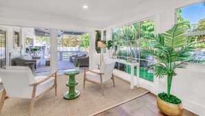 A bright, open living area with a large window, a green plant, and a white sofa. - Grand Residence | Heated Pool | Beach Proximity | Emerald Key | RESlDENCES (West Palm Beach)