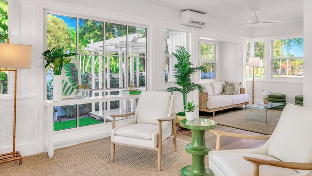 A spacious living room with large windows, a white sofa, a green coffee table, and a white armchair. - Grand Residence | Heated Pool | Beach Proximity | Emerald Key | RESlDENCES (West Palm Beach)