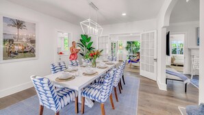 A spacious dining area with a long white table, blue patterned chairs, and a modern chandelier. - Grand Residence | Heated Pool | Beach Proximity | Emerald Key | RESlDENCES (West Palm Beach)