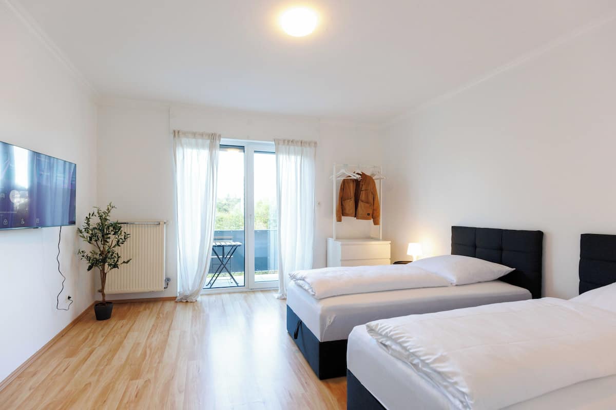 Habitación de hotel con dos camas, televisión, planta en maceta y vista al exterior por una puerta corrediza.