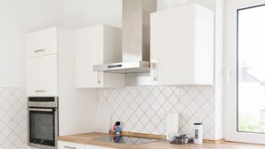 A modern kitchen with white cabinetry, a stainless steel oven, a wooden countertop, and a window providing natural light. - Apartmenthaus - Kaiserslautern (Kaiserslautern)