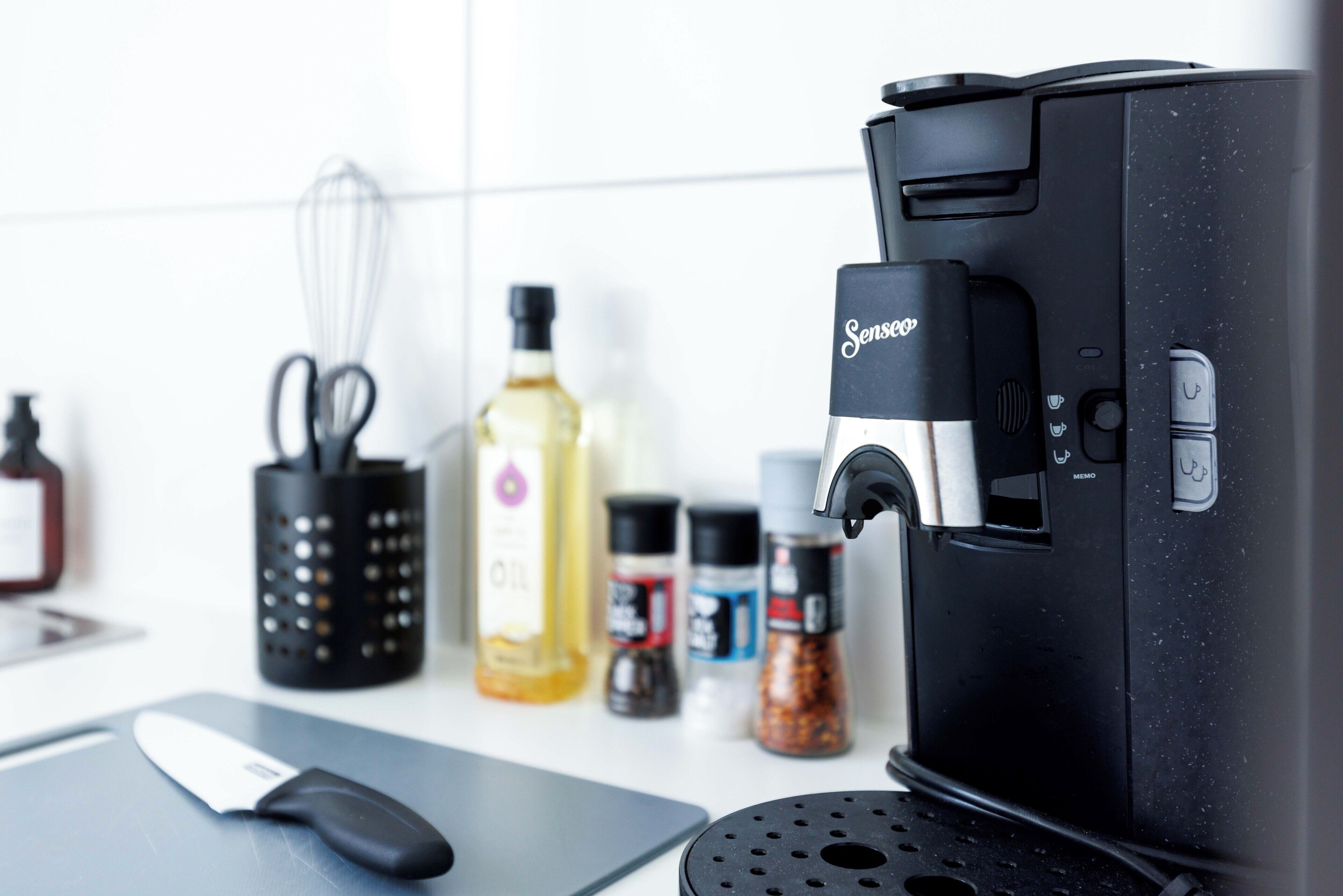 A kitchen counter with a coffee maker, a whisk, and various condiments.