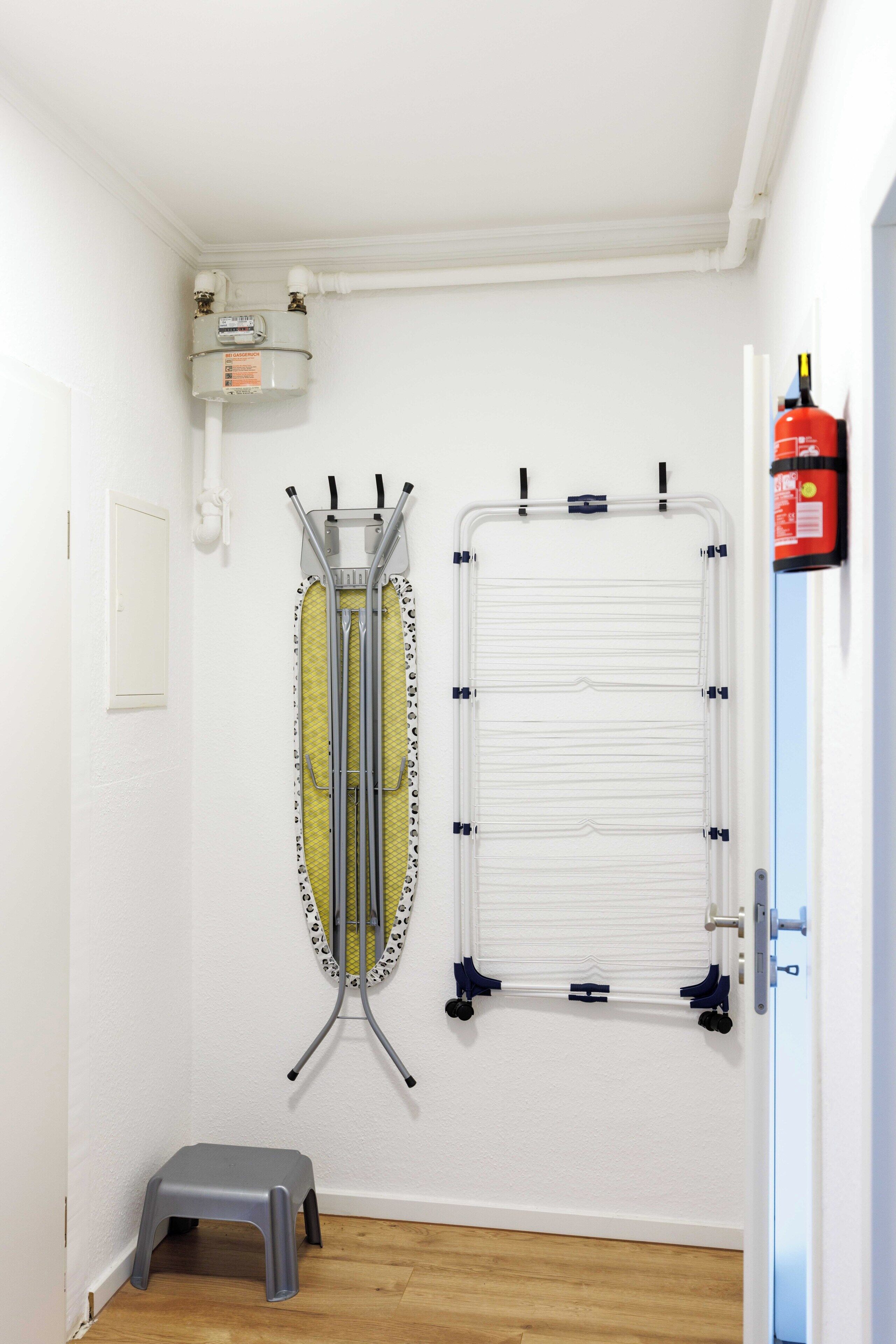 A room with a white door, a step stool, a wall-mounted ironing board, and a fire extinguisher.
