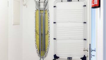 A room with a white door, a step stool, a wall-mounted ironing board, and a fire extinguisher.