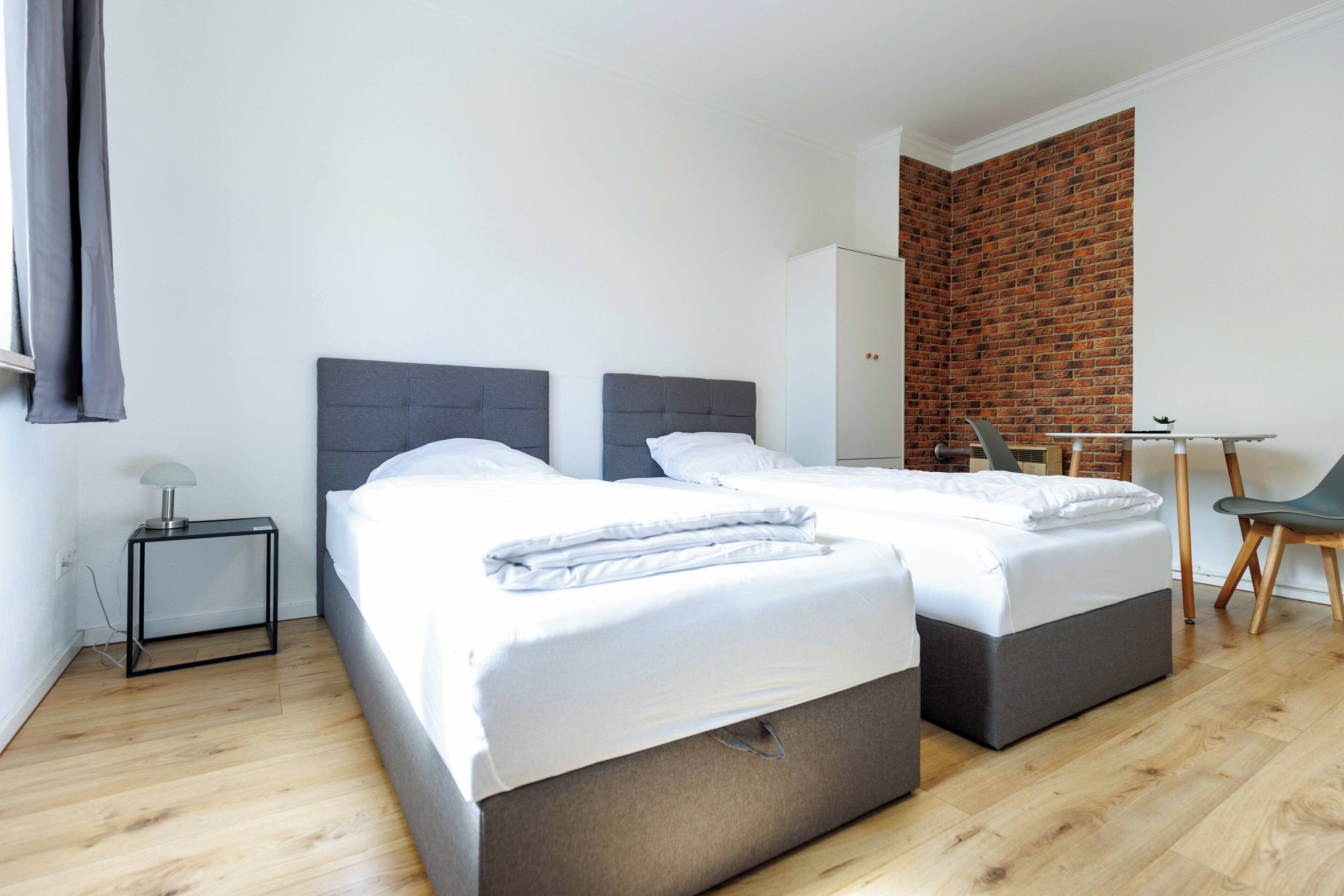 Une chambre d’hôtel moderne avec deux lits, une petite table, une chaise et un mur décoratif en briques.
