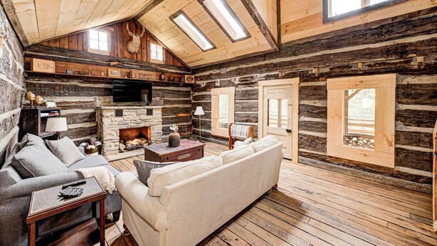 L’intérieur d’une cabane en rondins, avec une cheminée, un plancher en bois, un canapé et un téléviseur.