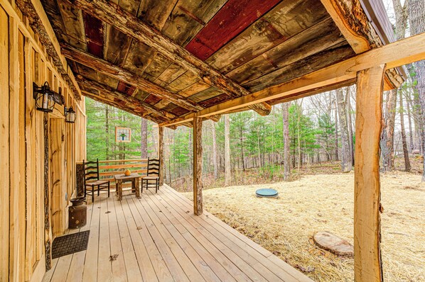 Una terraza de madera con techo rústico, una mesa con sillas y vistas a un bosque.