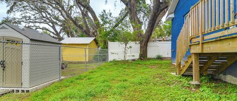 A fenced backyard with a small shed, a wooden deck, and a tree.