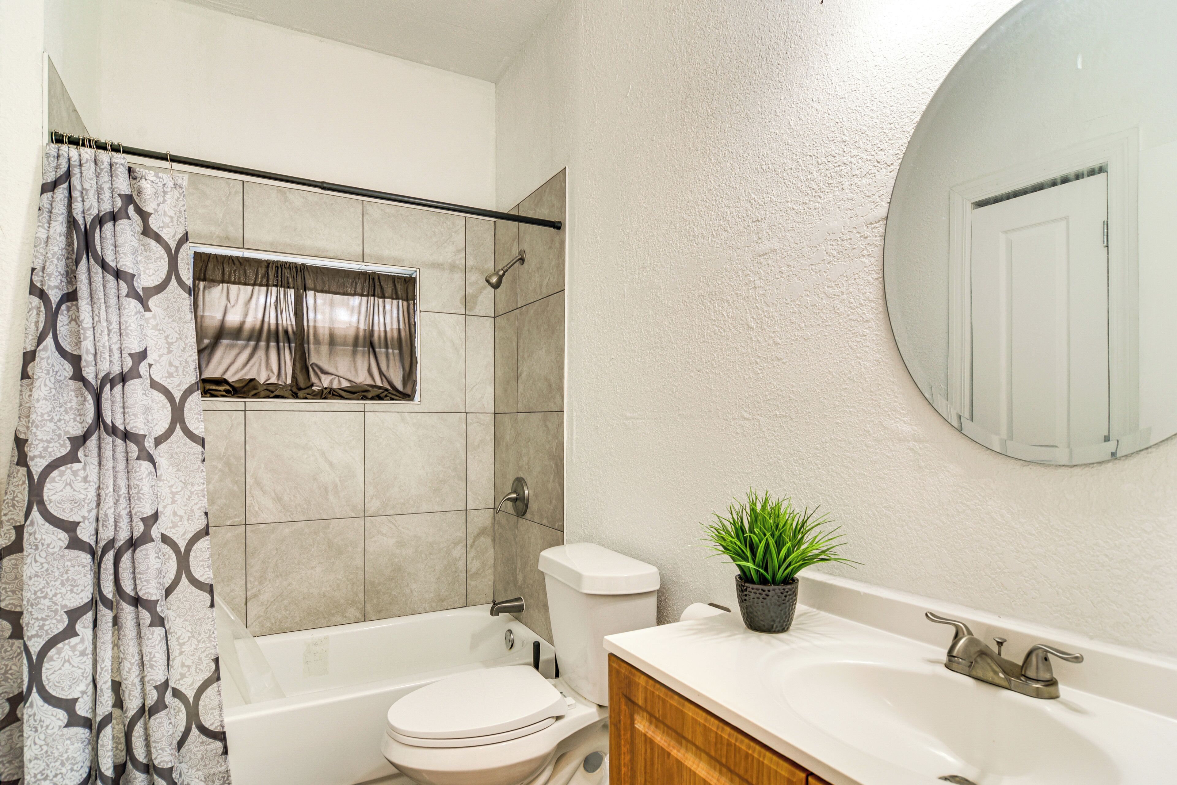 A bathroom with a bathtub, toilet, and sink, featuring a shower curtain, a potted plant, and a mirror on the wall.