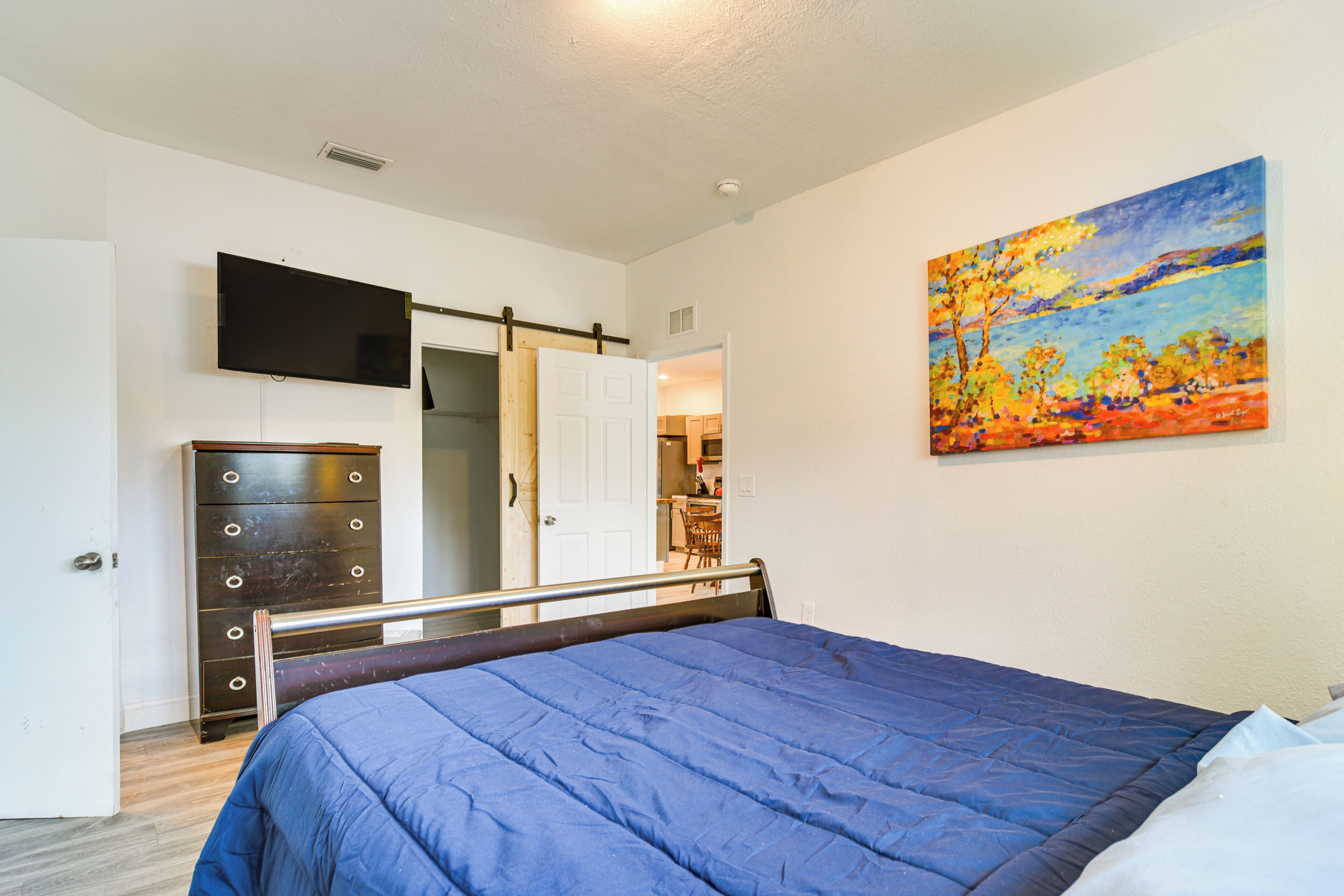 Un dormitorio con cama, cómoda, televisor y un cuadro en la pared.