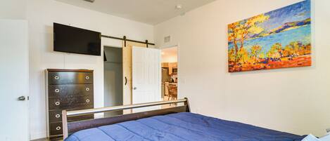 Un dormitorio con cama, cómoda, televisor y un cuadro en la pared.