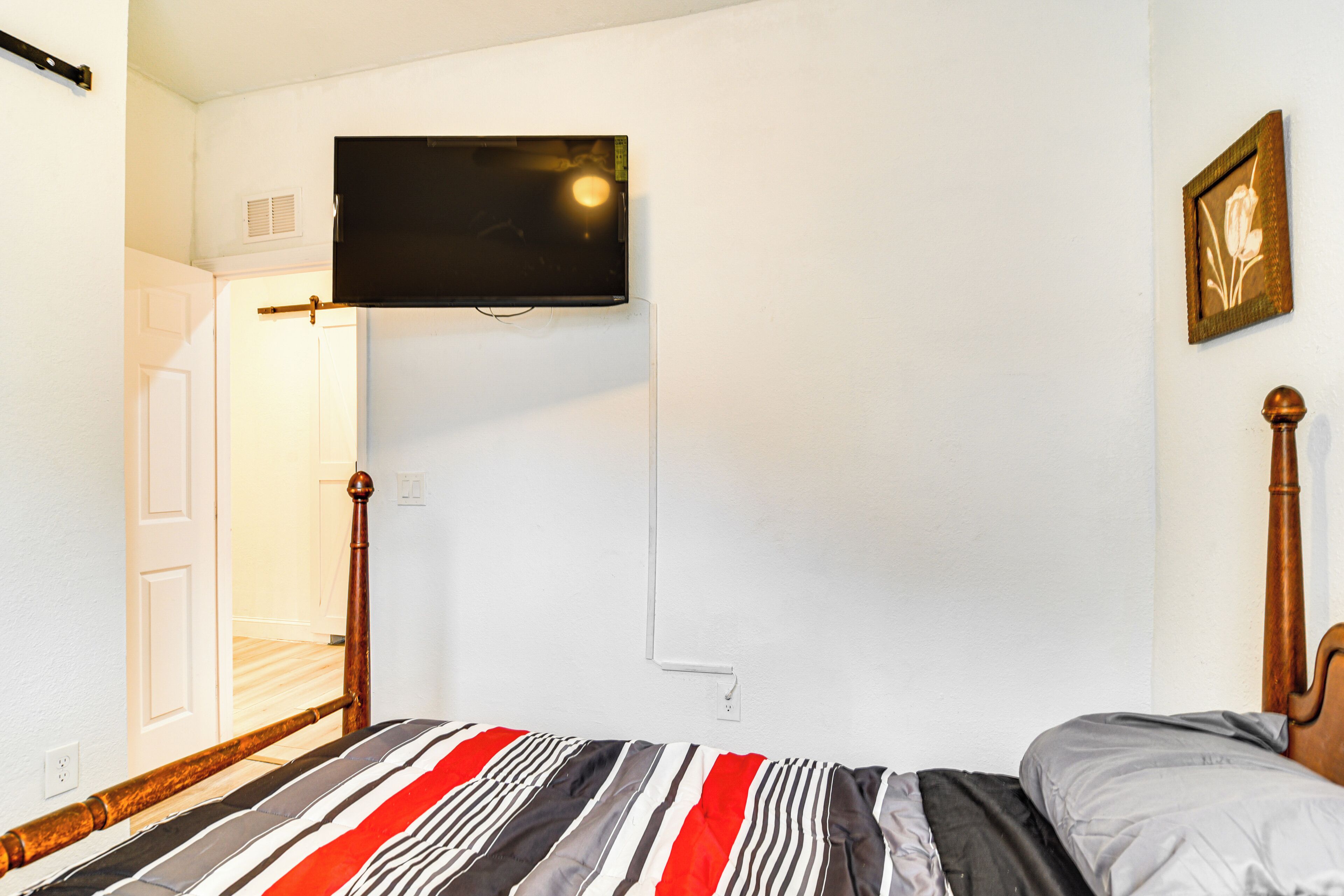 A bedroom with a bed, a television mounted on the wall, and a door leading to another room.