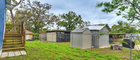 A backyard with a wooden deck, a shed, a fenced area, and a tree.