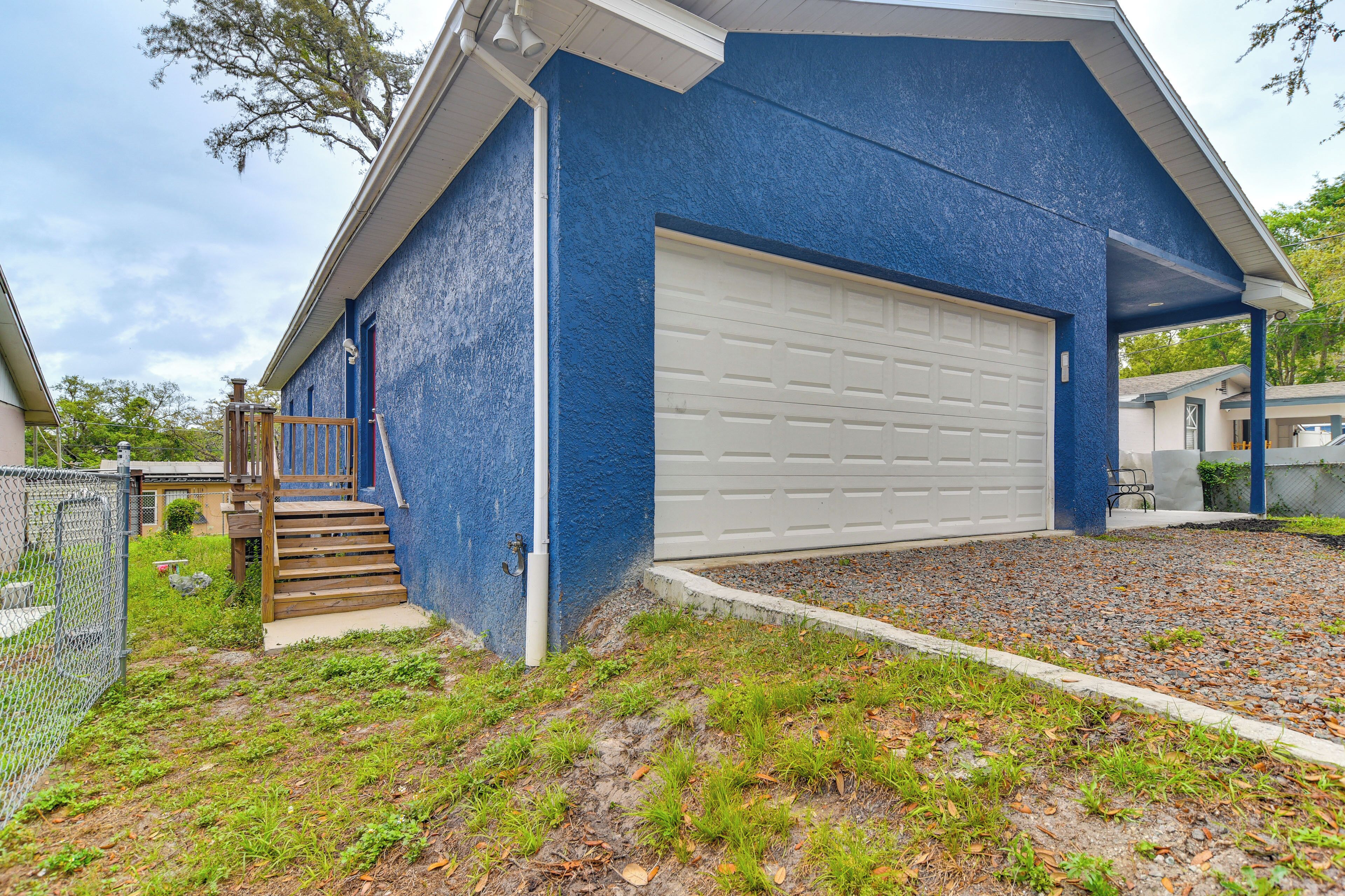 A blue building with a white garage door, a wooden staircase, and a gravel driveway.