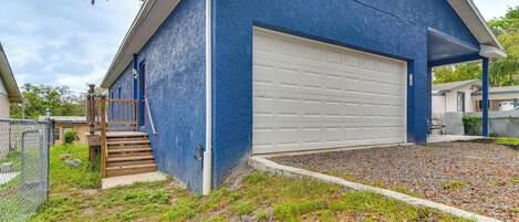 A blue building with a white garage door, a wooden staircase, and a gravel driveway.