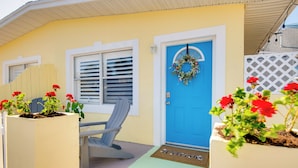 A yellow house with a blue door, a bench, and potted plants with red flowers.