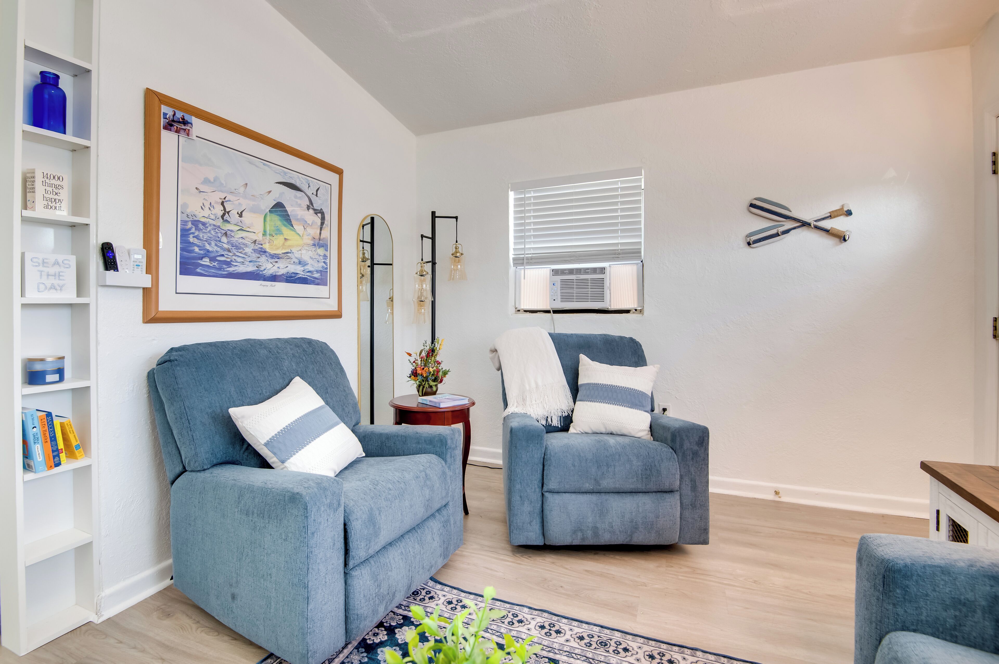 A living room with two blue armchairs, a bookshelf, a framed picture, and a window with blinds.