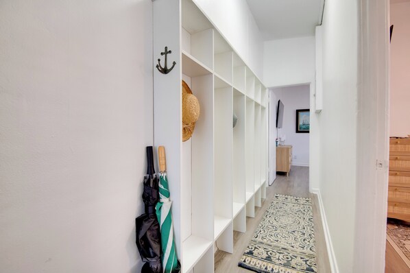 Un pasillo con estanterías blancas, un tapete estampado y una cesta colgante.